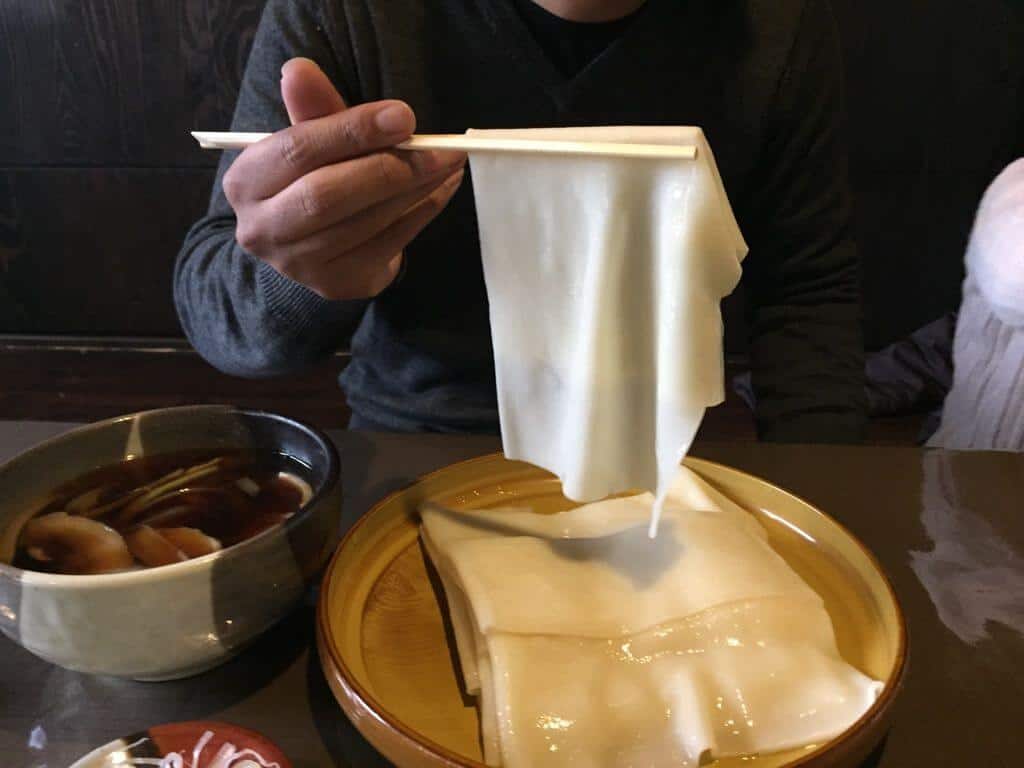 면과 찍어 먹는 소스가 담긴 접시 위에서 젓가락으로 집어 올린 얇고 리본 모양의 히모카와 우동 면