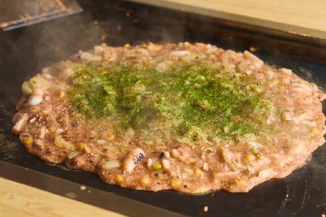 Monjayaki yang sudah matang di plat dengan taburan aonori
