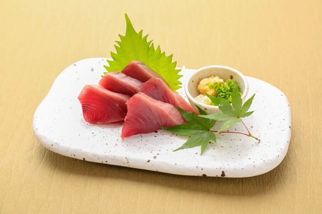 Tranches de sashimi de thon frais avec wasabi et feuilles vertes sur une assiette en céramique blanche, cuisine japonaise traditionnelle.