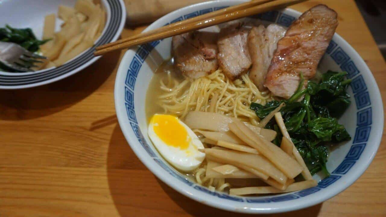Shio-Ramen mit geröstetem Schweinefleisch, weich gekochtem Ei, Menma und Spinat in einer Schüssel mit blauem Rand