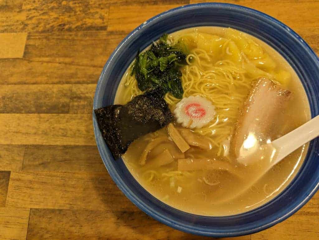 Hakodate-Ramen mit Nori, Naruto, Chashu und Spinat in einer blauen Schüssel auf einem Holztisch