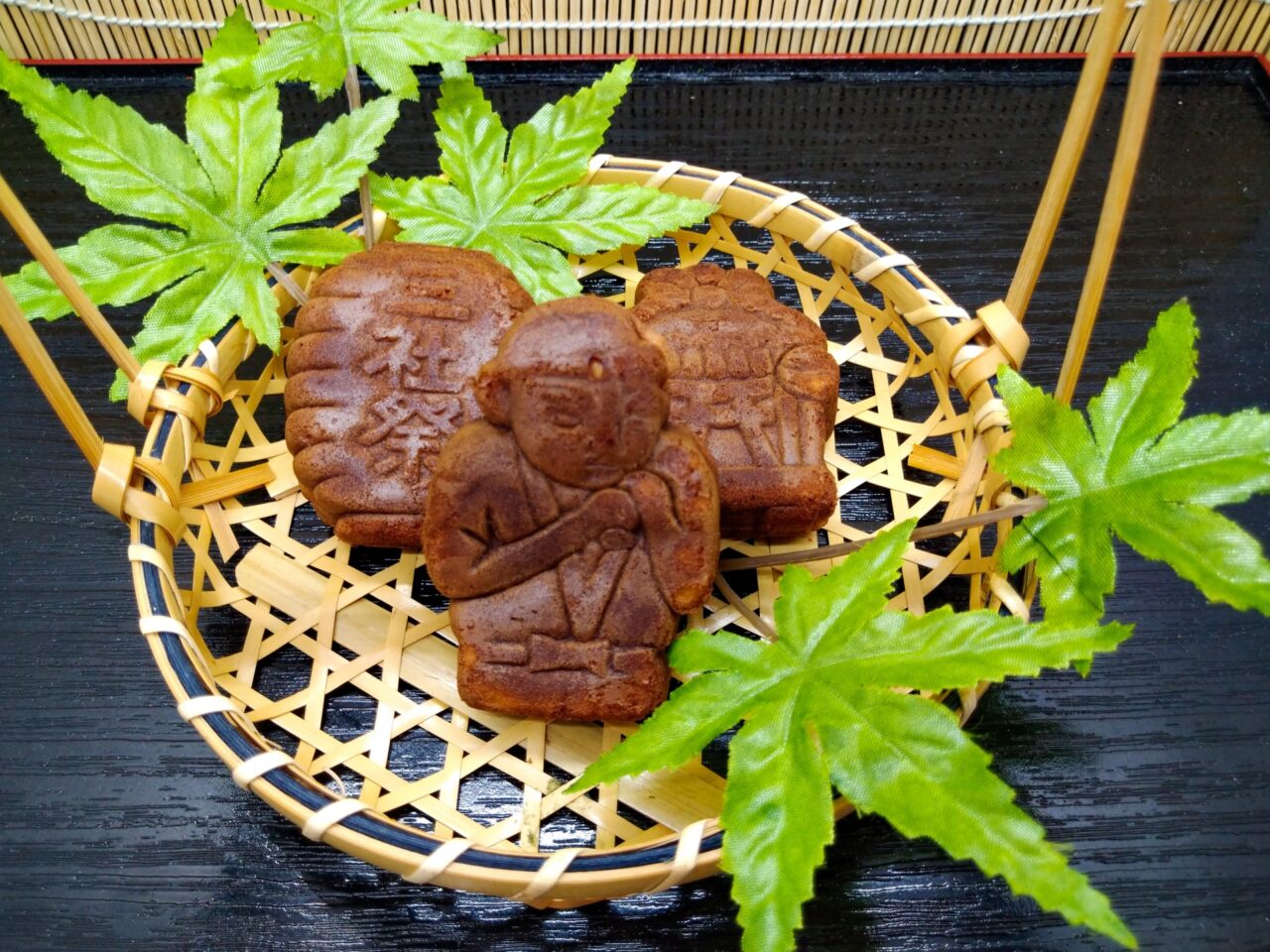 Sweet Ningyo yaki cookies shaped like traditional Japanese dolls, served on a bamboo tray with green.
