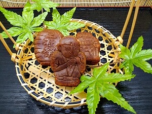 Sweet Ningyo yaki cookies shaped like traditional Japanese dolls, served on a bamboo tray with green.