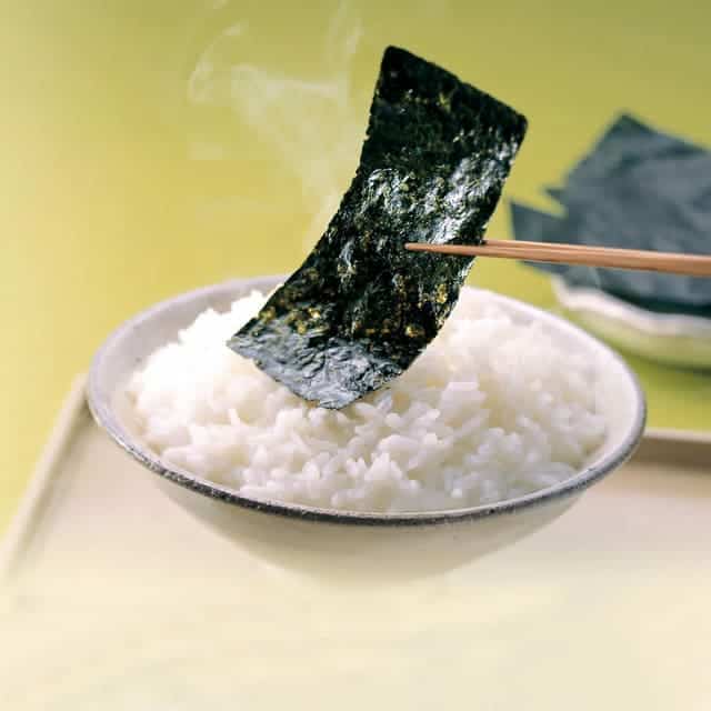 Toasted Seaweed or Nori being held by chopsticks on top of rice