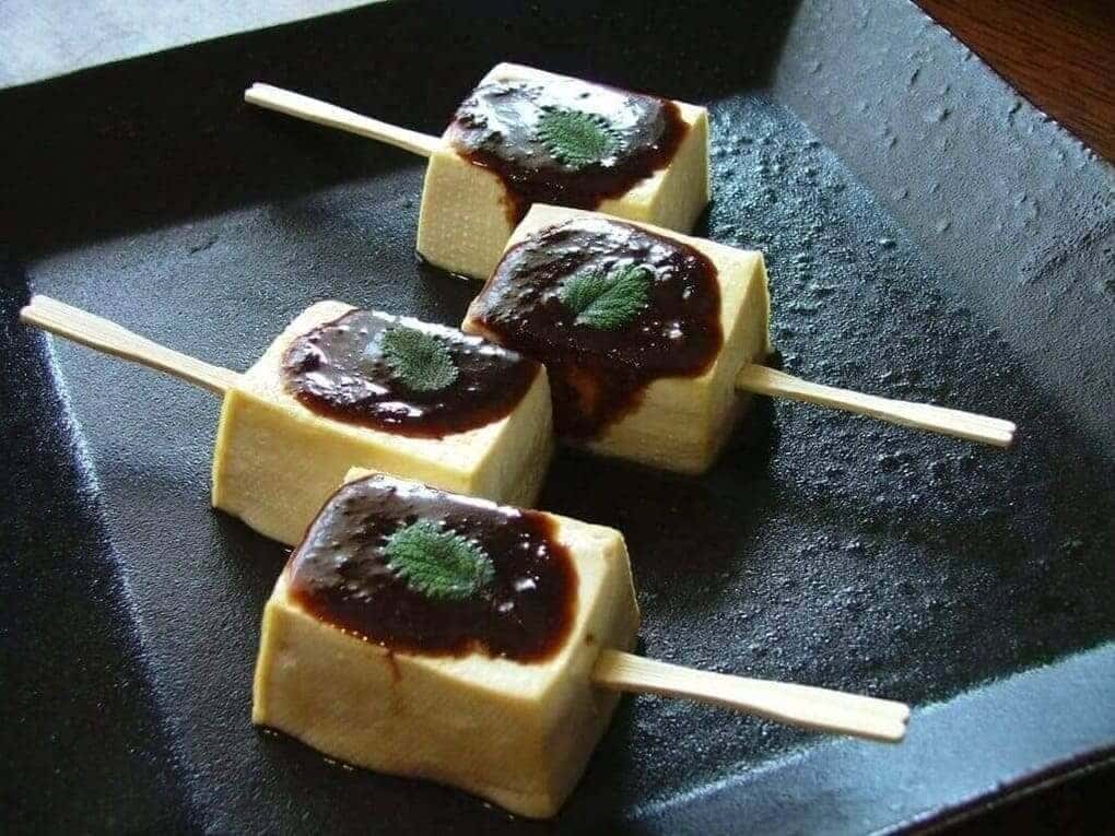 Tofu dengaku with sauce on top on a black plate