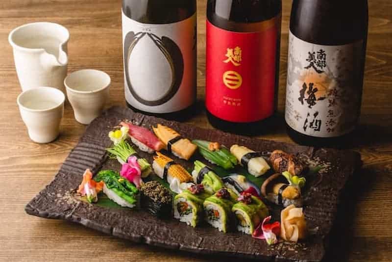 Assorted Japanese sushi with sake bottles on a rustic wooden table.