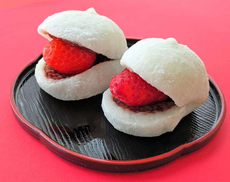 Fresh strawberry daifuku mochi on a black plate, showcasing traditional Japanese sweet treats.