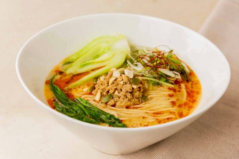 Creamy miso ramen with ground meat, fresh vegetables, and chili oil in a white bowl for authentic Japanese cuisine.