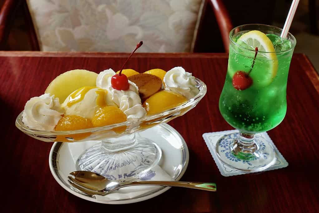 Colorful Japanese-style fruit dessert with whipped cream and cherry paired with a refreshing lemon-lime soda.