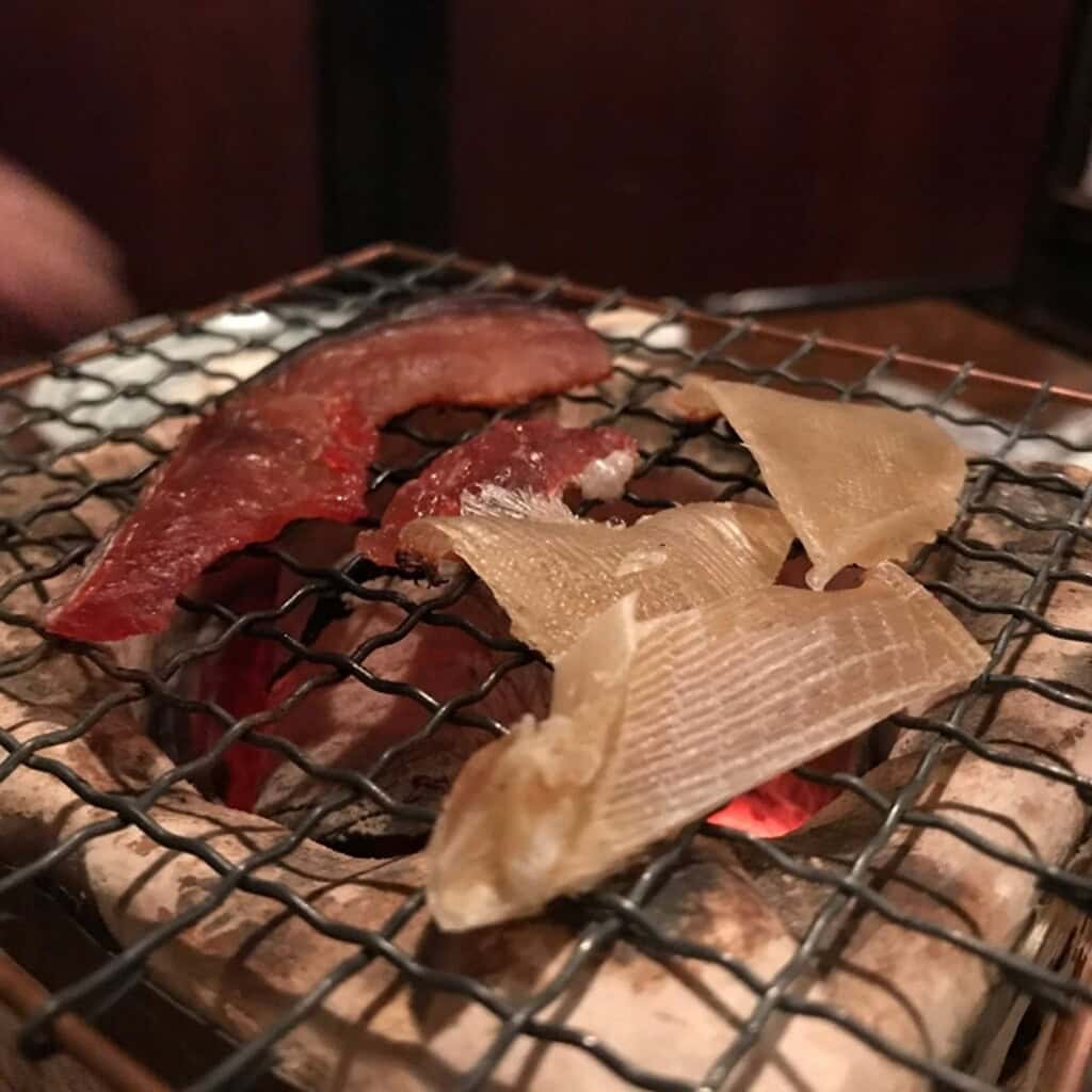 Grilled stingray fin (eihire) on a traditional Japanese grill, showcasing a popular seafood delicacy.