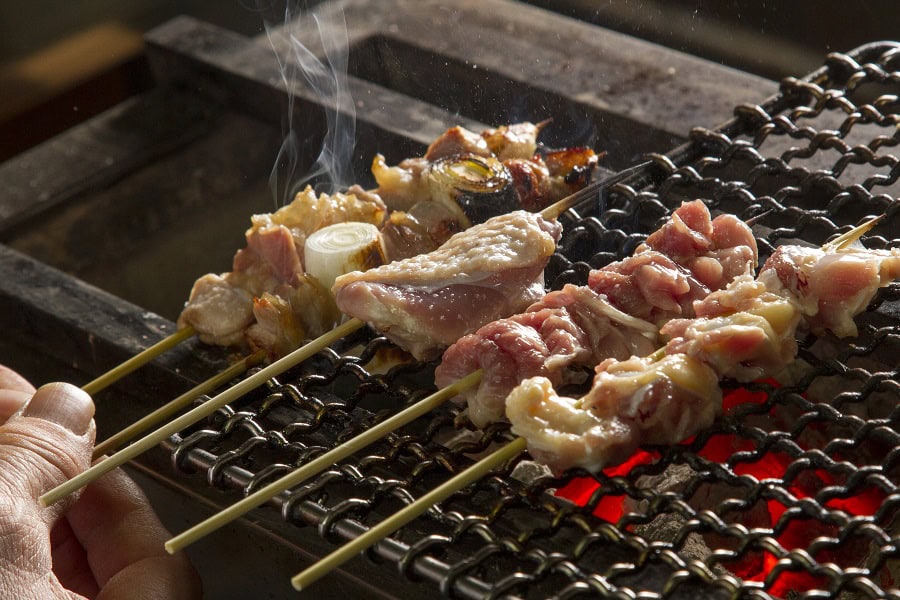 Skewers of grilled Okukuji Shamo chicken cooking over charcoal.