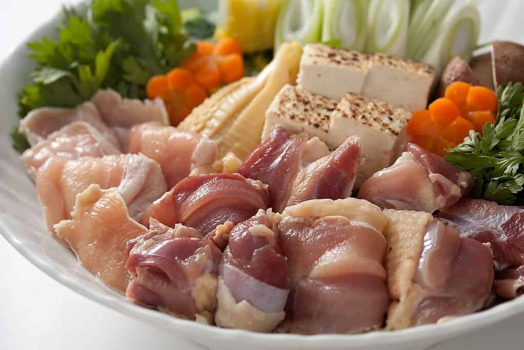 Fresh Okukuji Shamo chicken pieces with vegetables and tofu on a white plate.