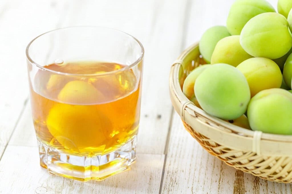 Glass of Mito Umeshu with fresh green plums in a basket.