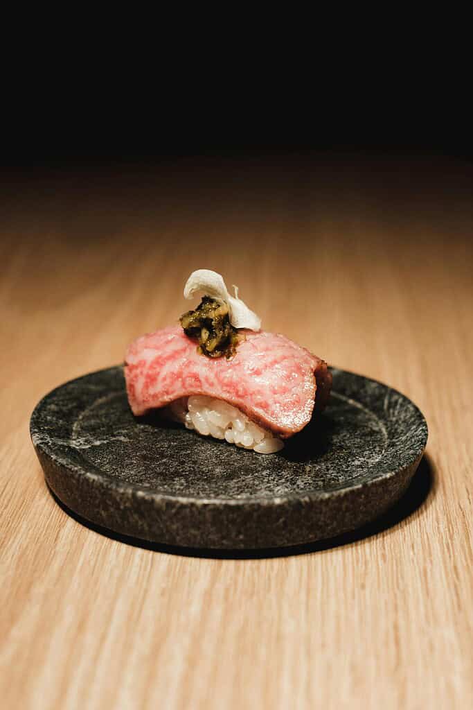 Premium Tajima beef sushi with rice on a black plate, close-up.