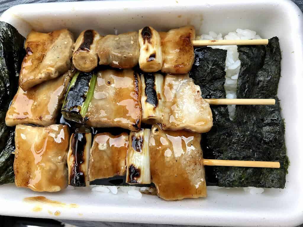 Delicious grilled chicken skewers with rice and seaweed in a traditional Japanese bento box.