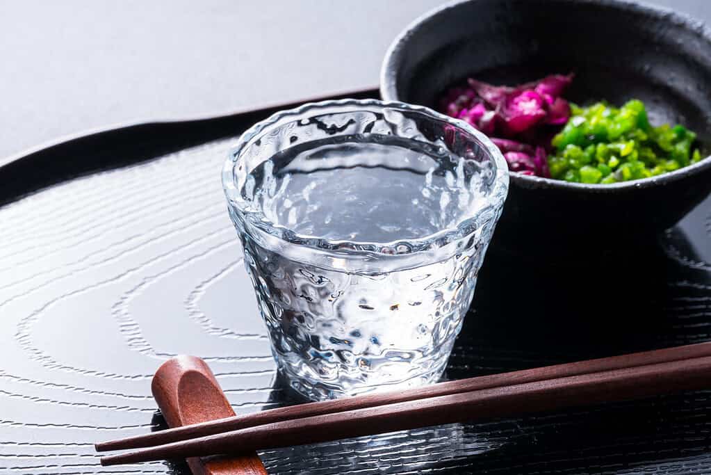Traditional Japanese meal with a glass of water, pickled vegetables, and chopsticks on a black tray.