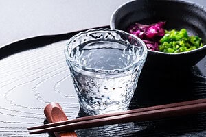 Traditional Japanese meal with a glass of water, pickled vegetables, and chopsticks on a black tray.