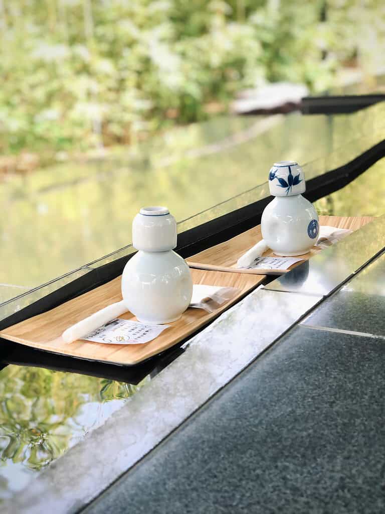 Traditional Japanese sake bottles on wooden trays by a river in Kyoto, Japan.