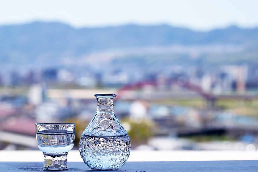 Clear glass water pitcher and glass on a balcony with a cityscape and mountains in the background.