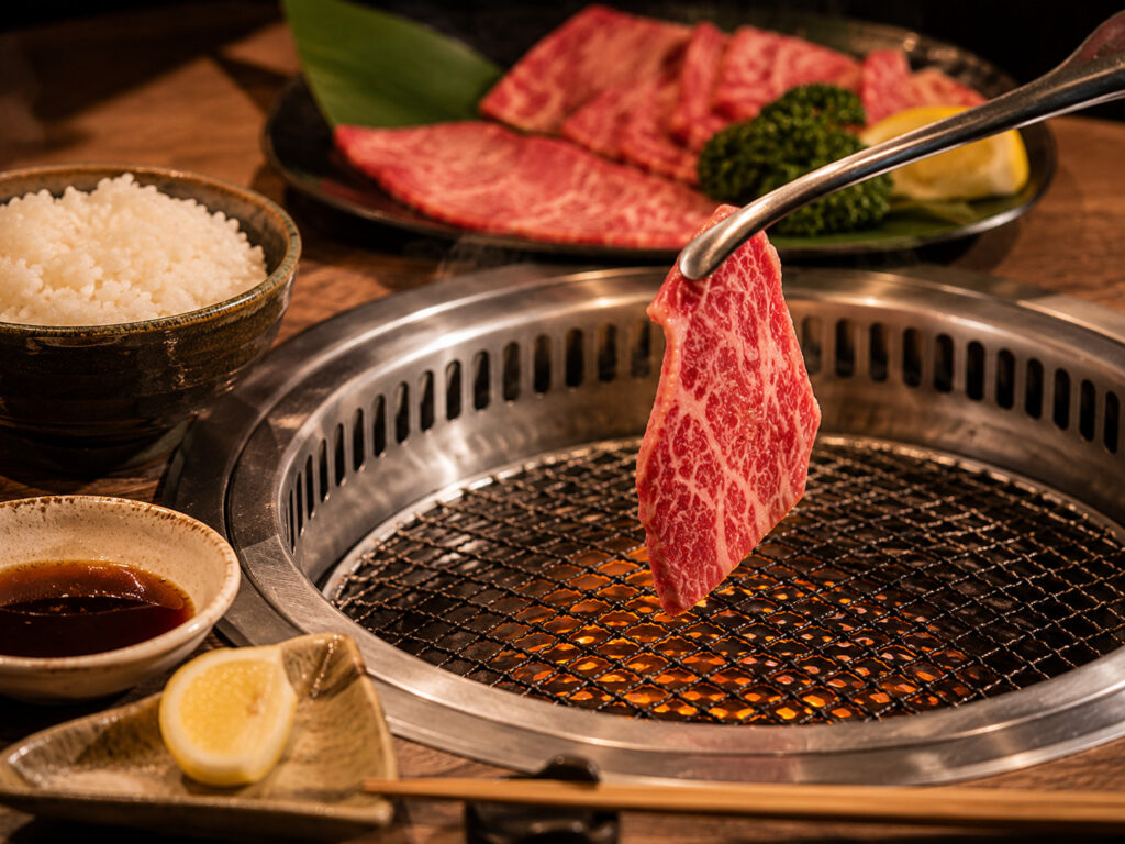 Tongs placing beef on a Japanese yakiniku tabletop grill