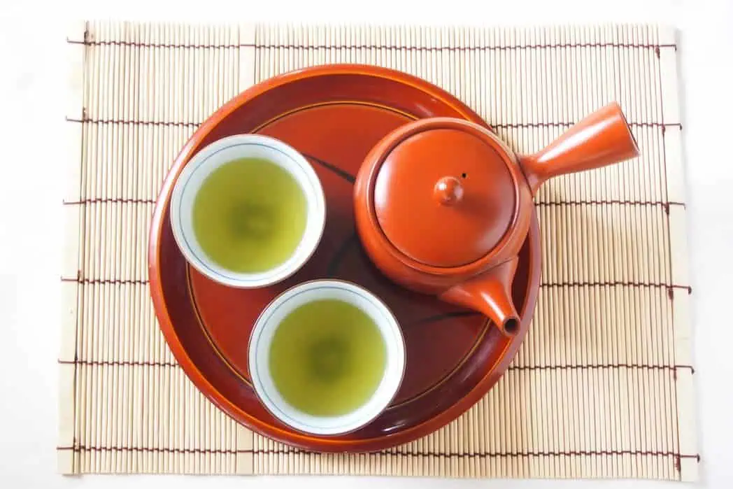 Traditional Japanese green tea served in two cups with a teapot on a bamboo mat.
