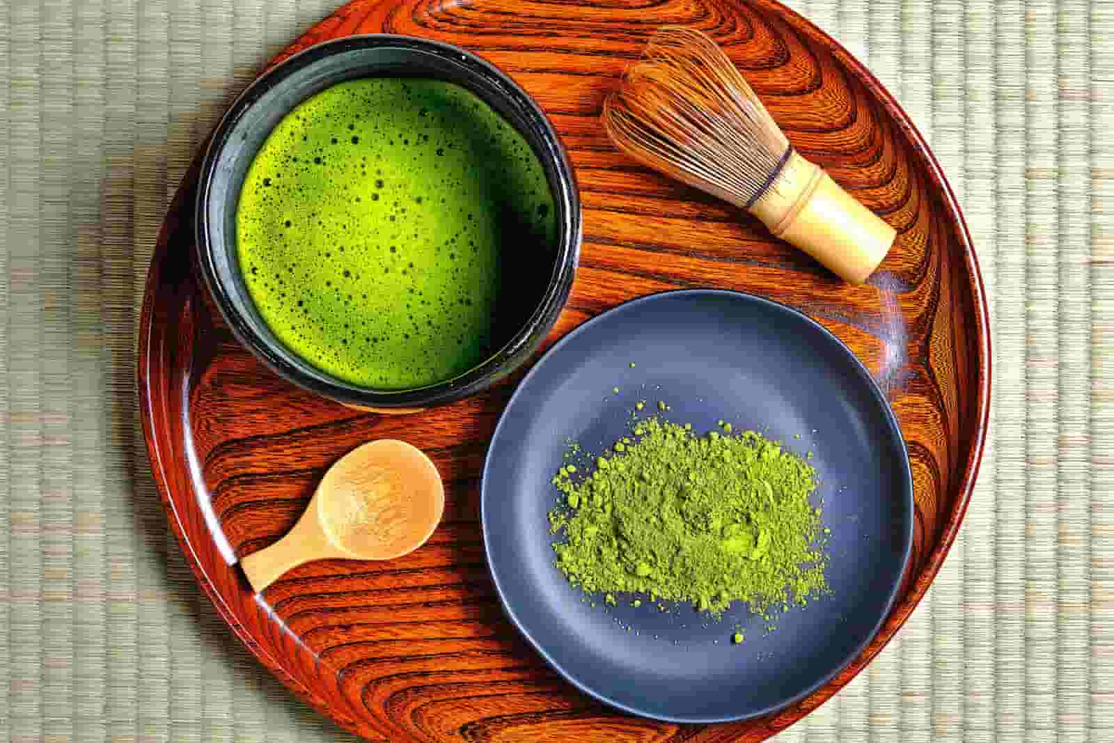 Traditional ceremonial matcha tea with whisk and powdered tea on wooden tray.