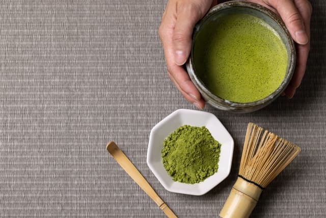 Traditional Japanese ceremonial matcha tea in a bowl with whisk and powdered matcha.