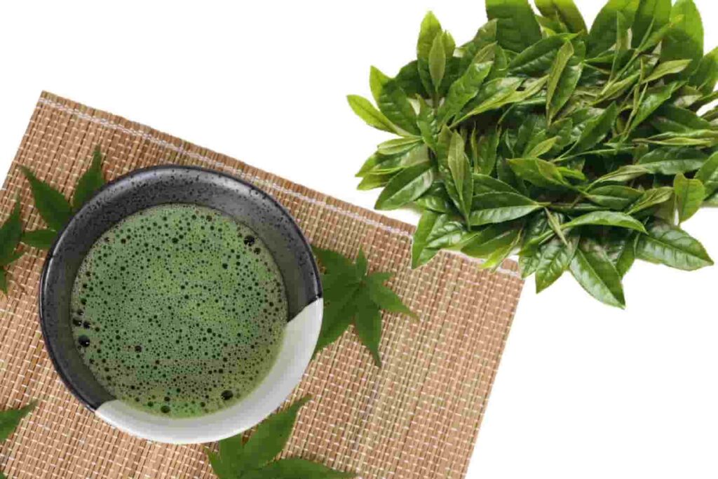 Fresh green matcha tea with tea leaves on a bamboo mat.