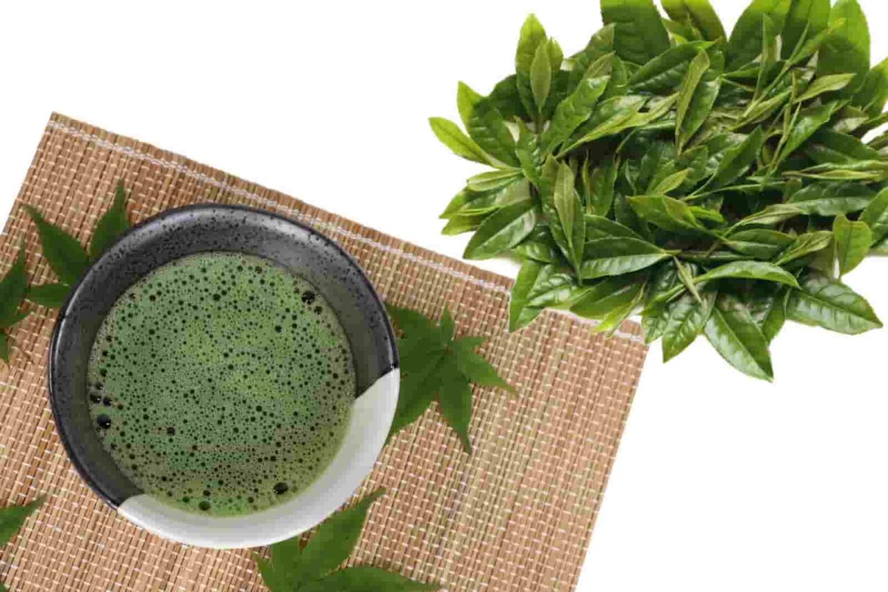 Fresh green matcha tea with tea leaves on a bamboo mat.