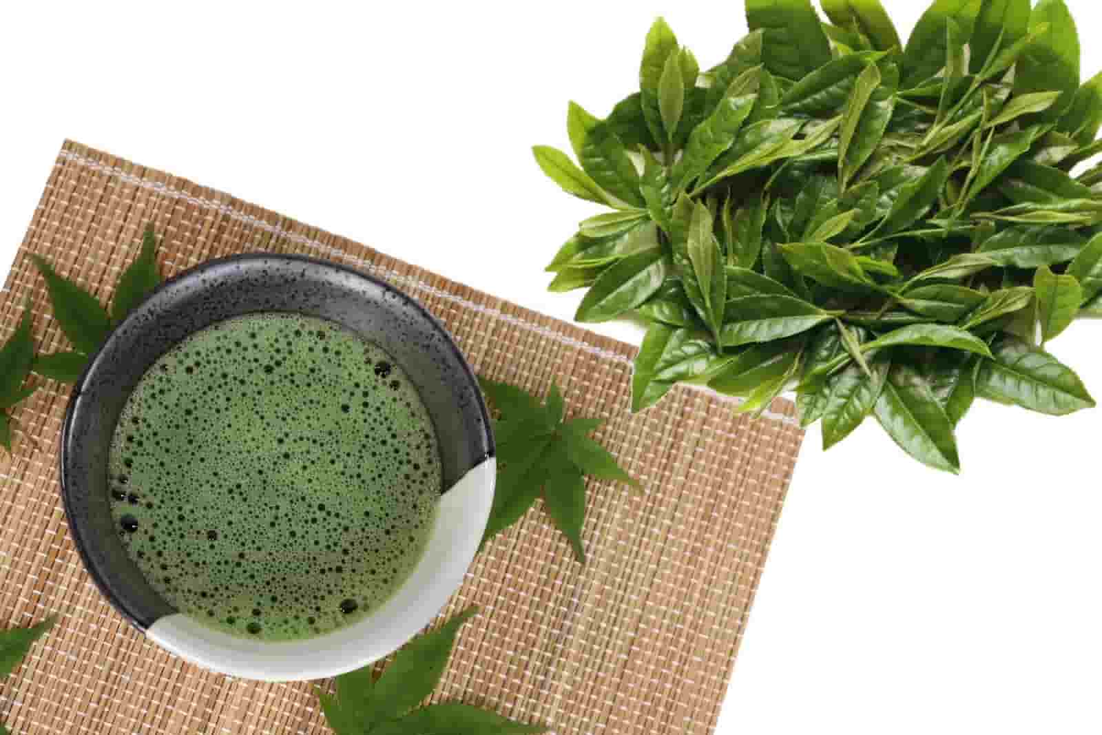 Fresh green matcha tea with tea leaves on a bamboo mat.