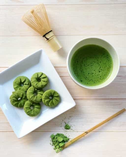 Traditional Japanese matcha tea with green sweets and bamboo whisk on light wooden surface.