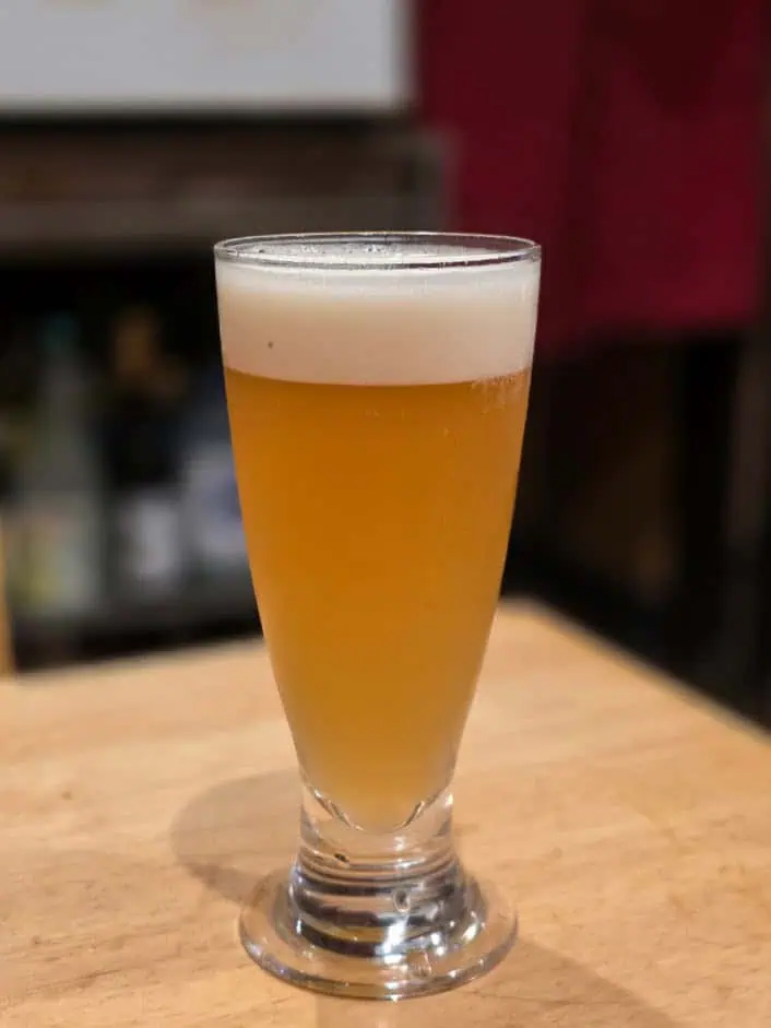 Glass of Shikuwasa drink with frothy top on a wooden table.