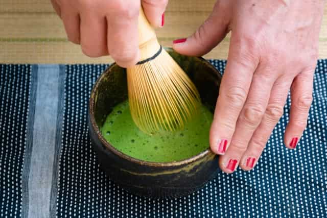 Traditional Japanese matcha tea being whisked in a bowl with a bamboo whisk.