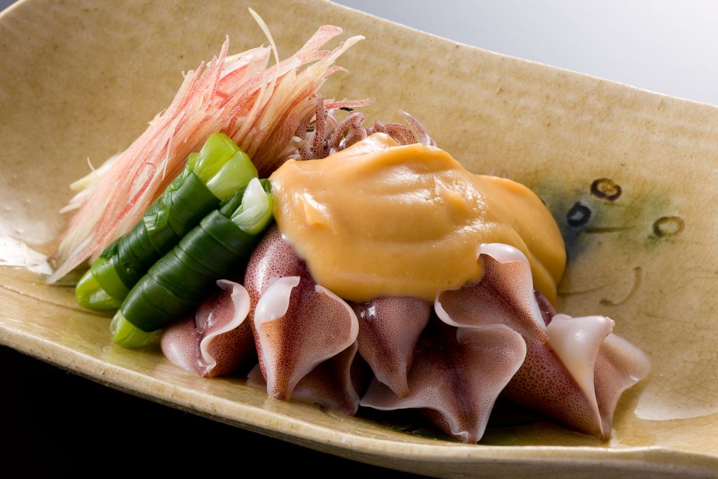 Fresh firefly squid sashimi with garnishes on a ceramic plate.