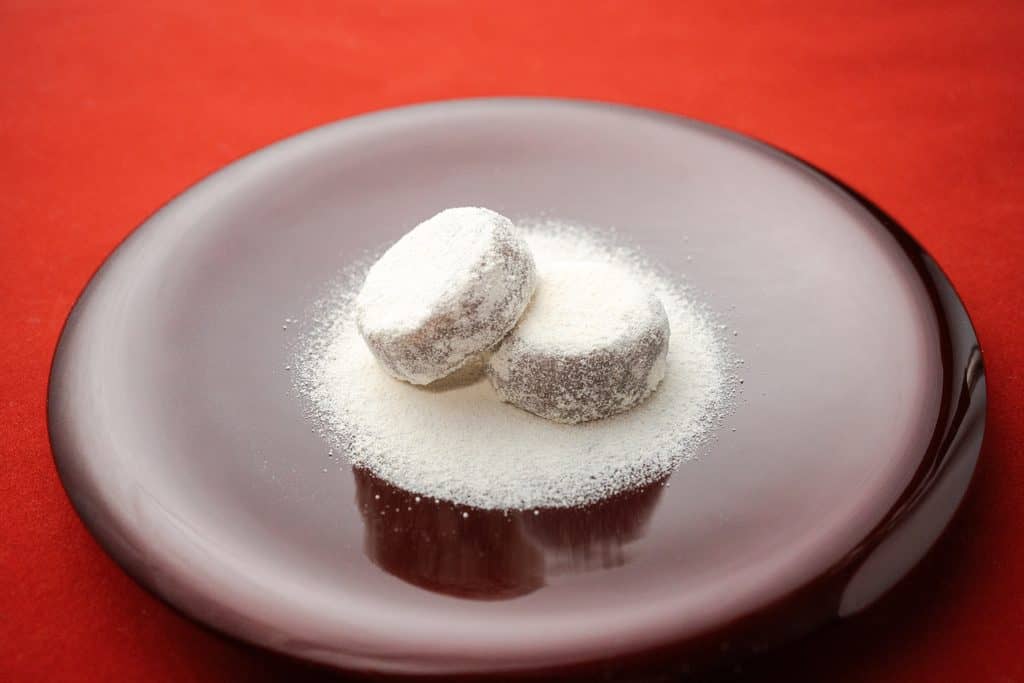 Japanese sweets with powdered sugar on a black plate against a red background.