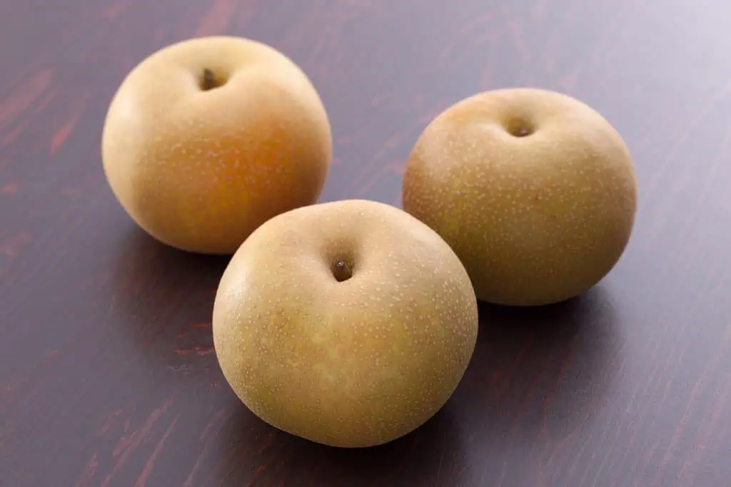 Three Kureha Nashi pears on a dark wooden surface.