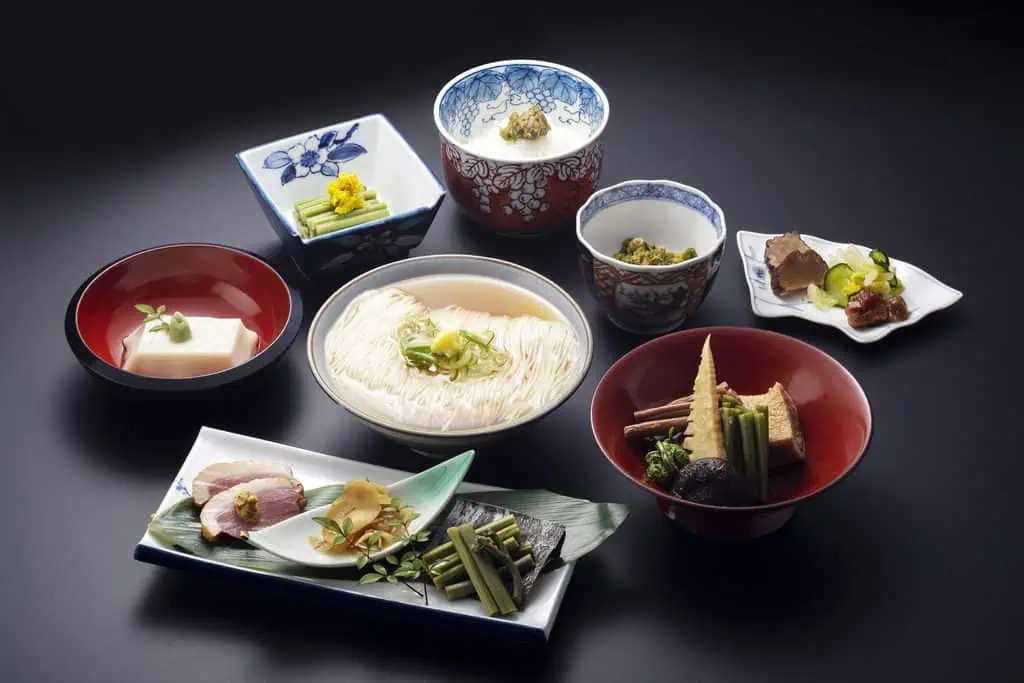 Traditional Japanese meal with somen noodles, sashimi, and side dishes on black background.