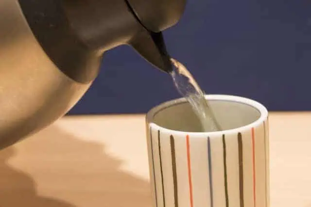 Pouring freshly brewed genmaicha into a striped ceramic cup, a traditional Japanese tea serving style.