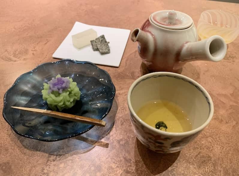 Kaga Bōcha served in a traditional Japanese tea setting with a ceramic teapot, cup of tea, and a wagashi sweet.