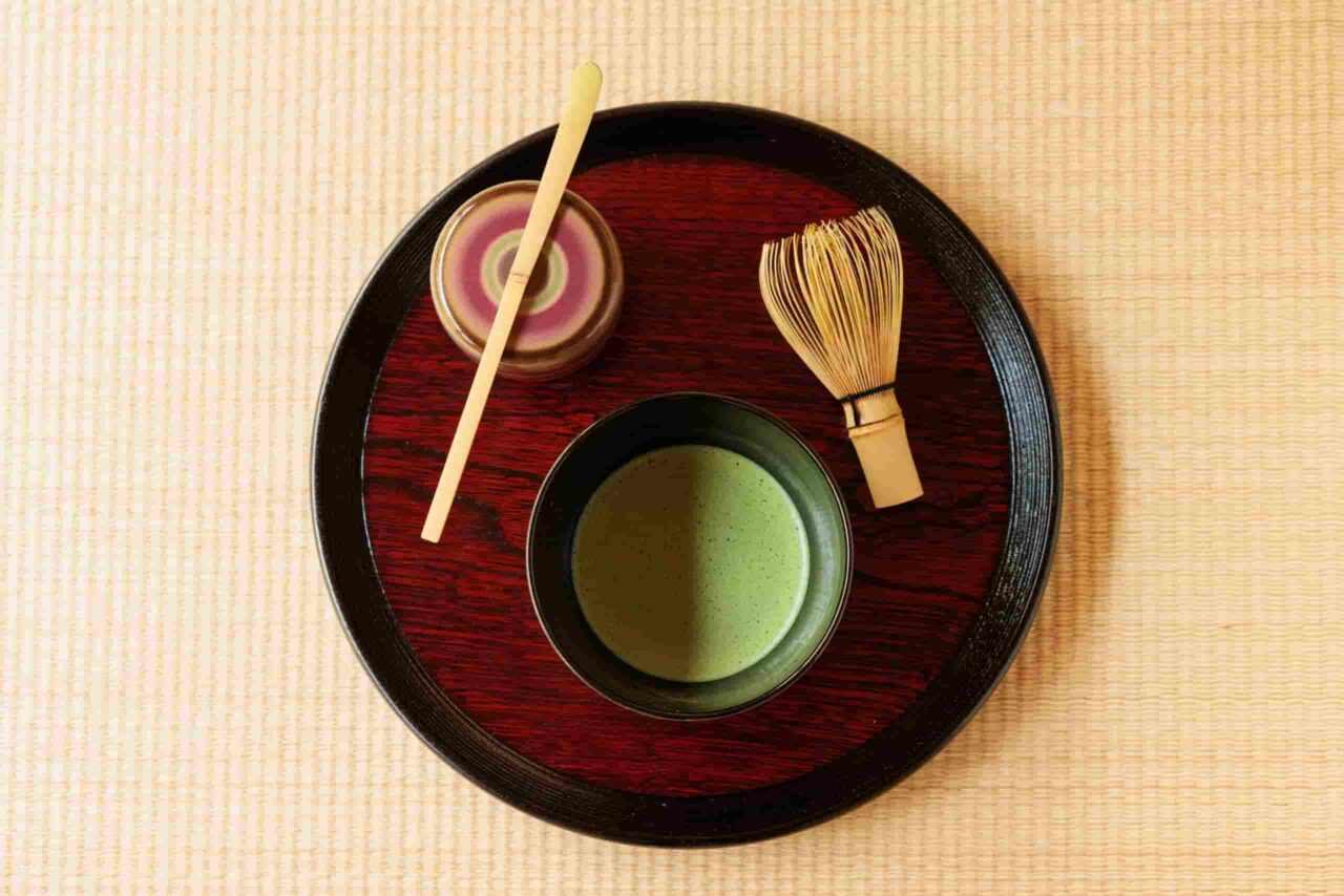 A bowl of usucha matcha tea with a bamboo whisk and matcha scoop on a traditional Japanese tea tray.