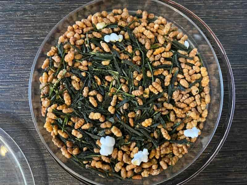 A bowl of genmaicha showing green tea leaves mixed with toasted brown rice and popped rice grains.