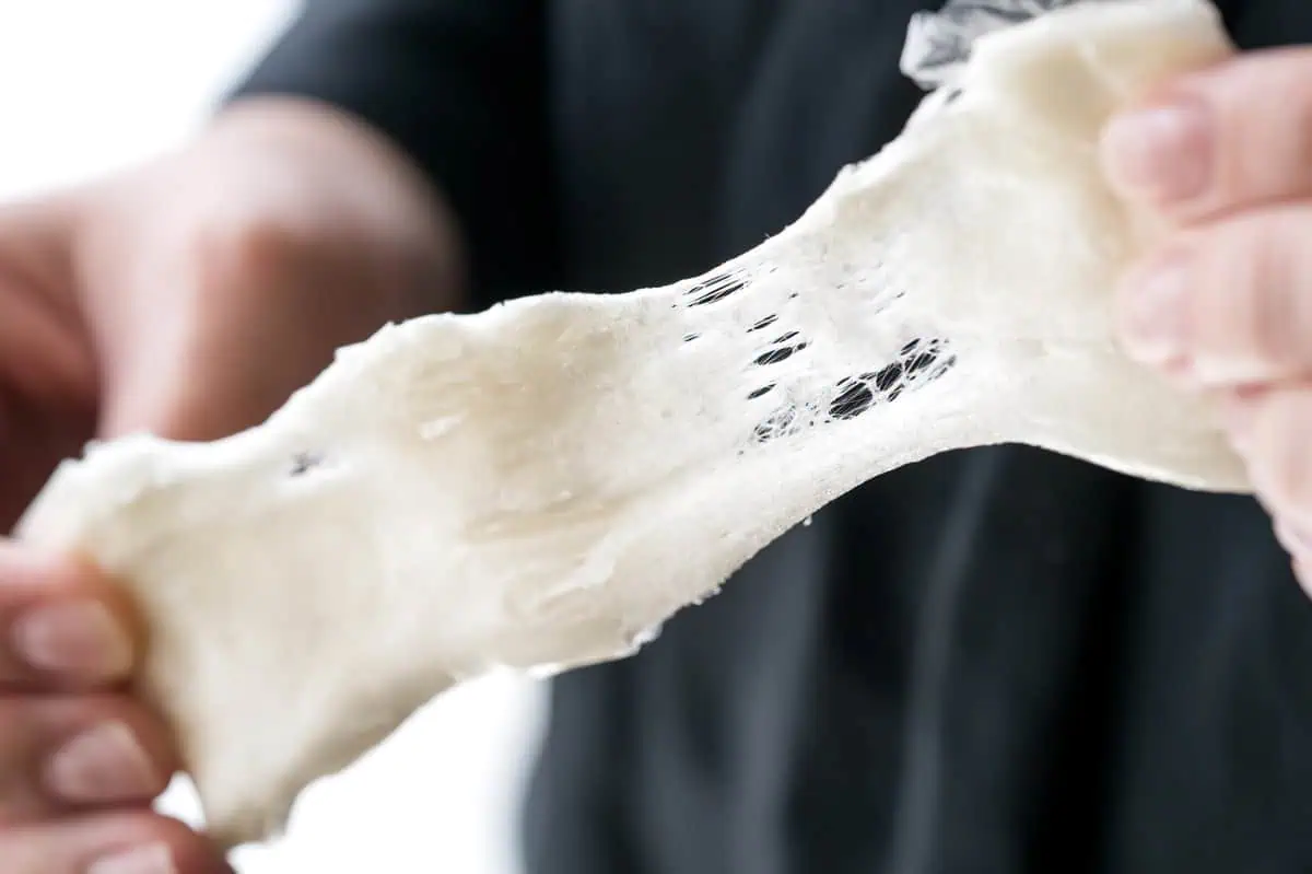 Hands stretching a pale amegata bar to show its fibrous, pulled texture