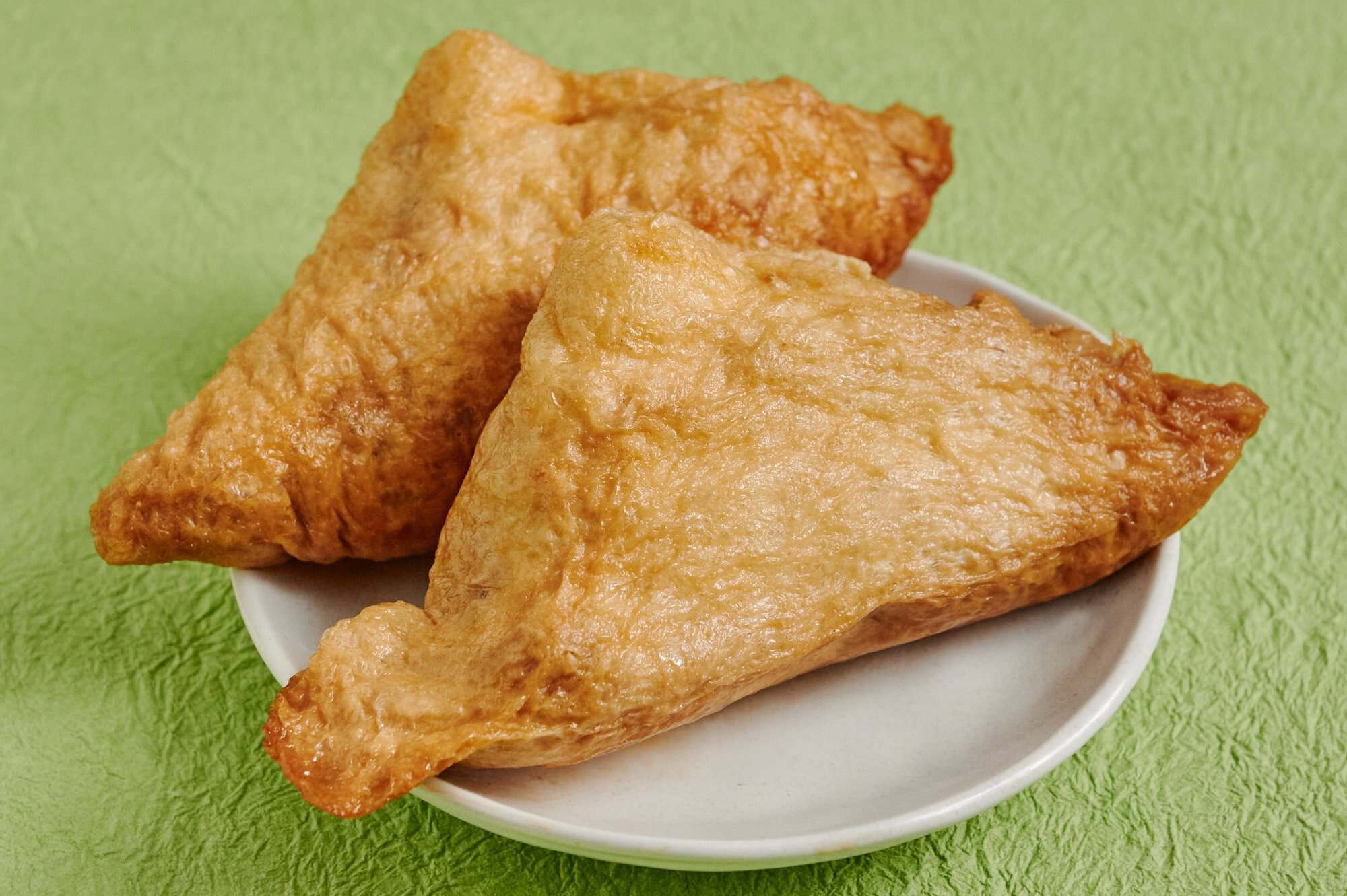Un itadaki abierto para mostrar el relleno de arroz sazonado, bardana, zanahoria y shiitake dentro de la bolsita de tofu frito