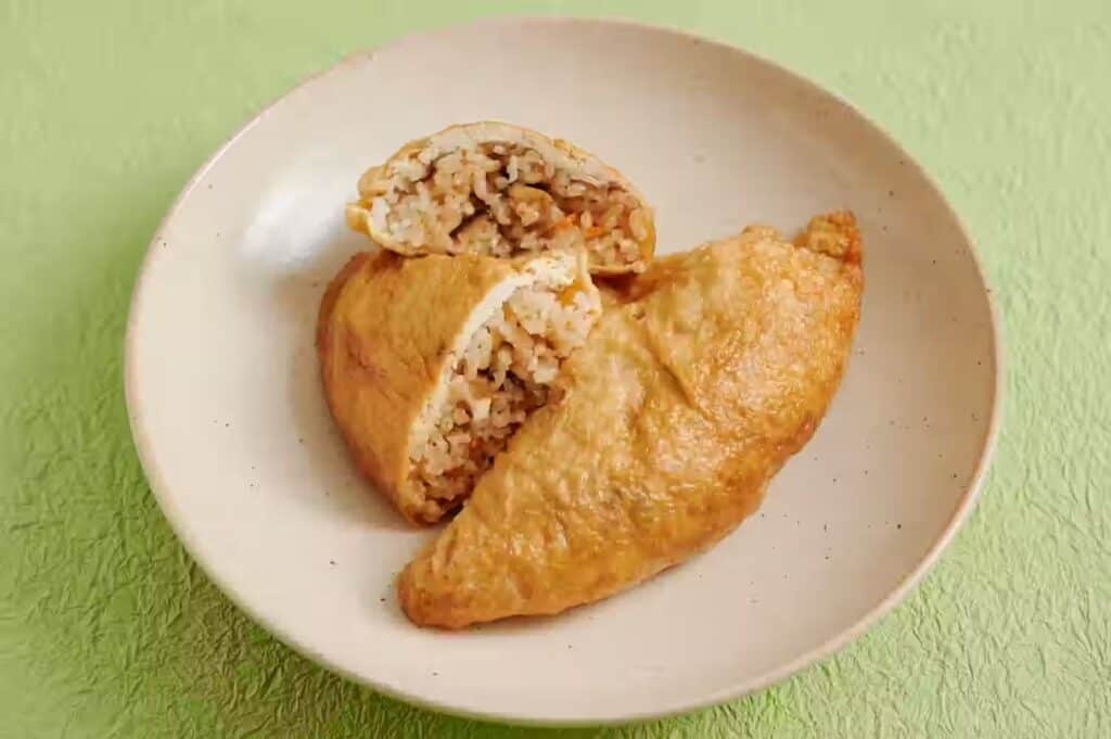 Two triangular itadaki, rice-stuffed fried tofu pouches, on a white plate against a green paper background