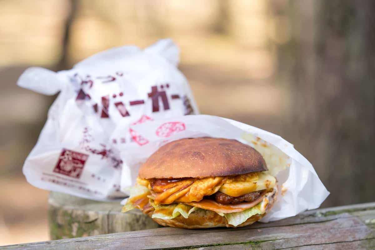 A Karatsu Burger half-wrapped in paper in front of its printed paper bag