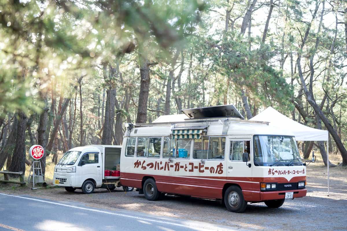The red and cream Karatsu Burger microbus parked among the pines of Nijinomatsubara