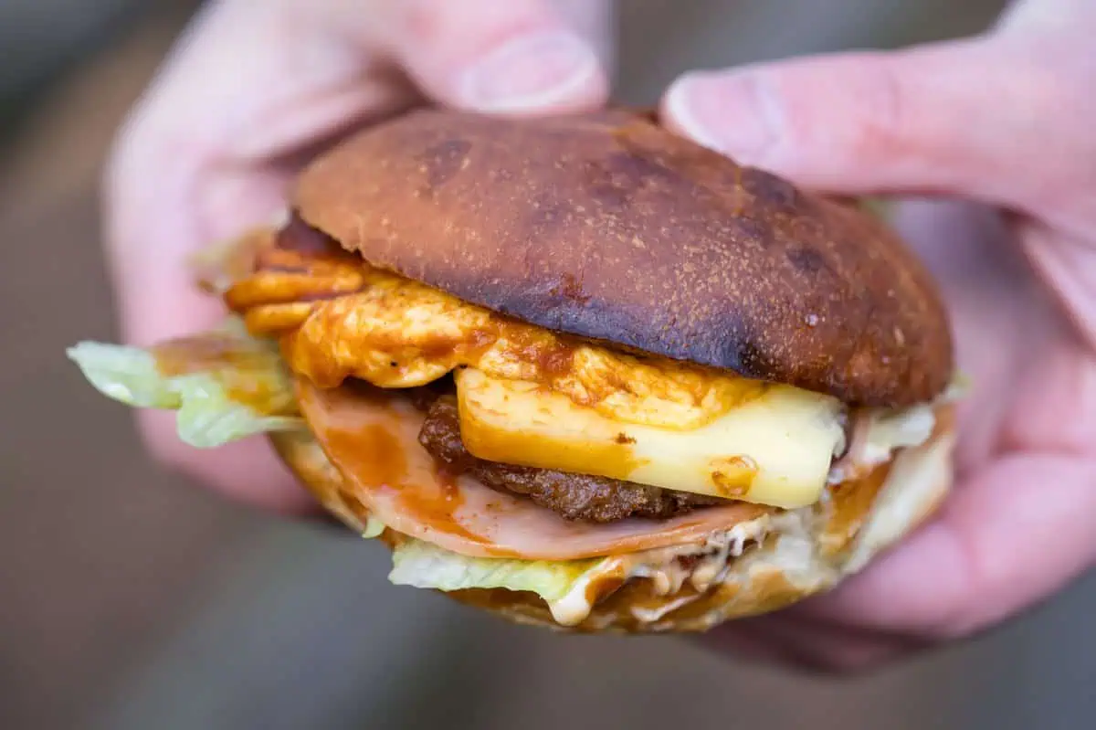 A hand holding a Karatsu Burger with egg, cheese, patty, ham, lettuce and demi-glace sauce