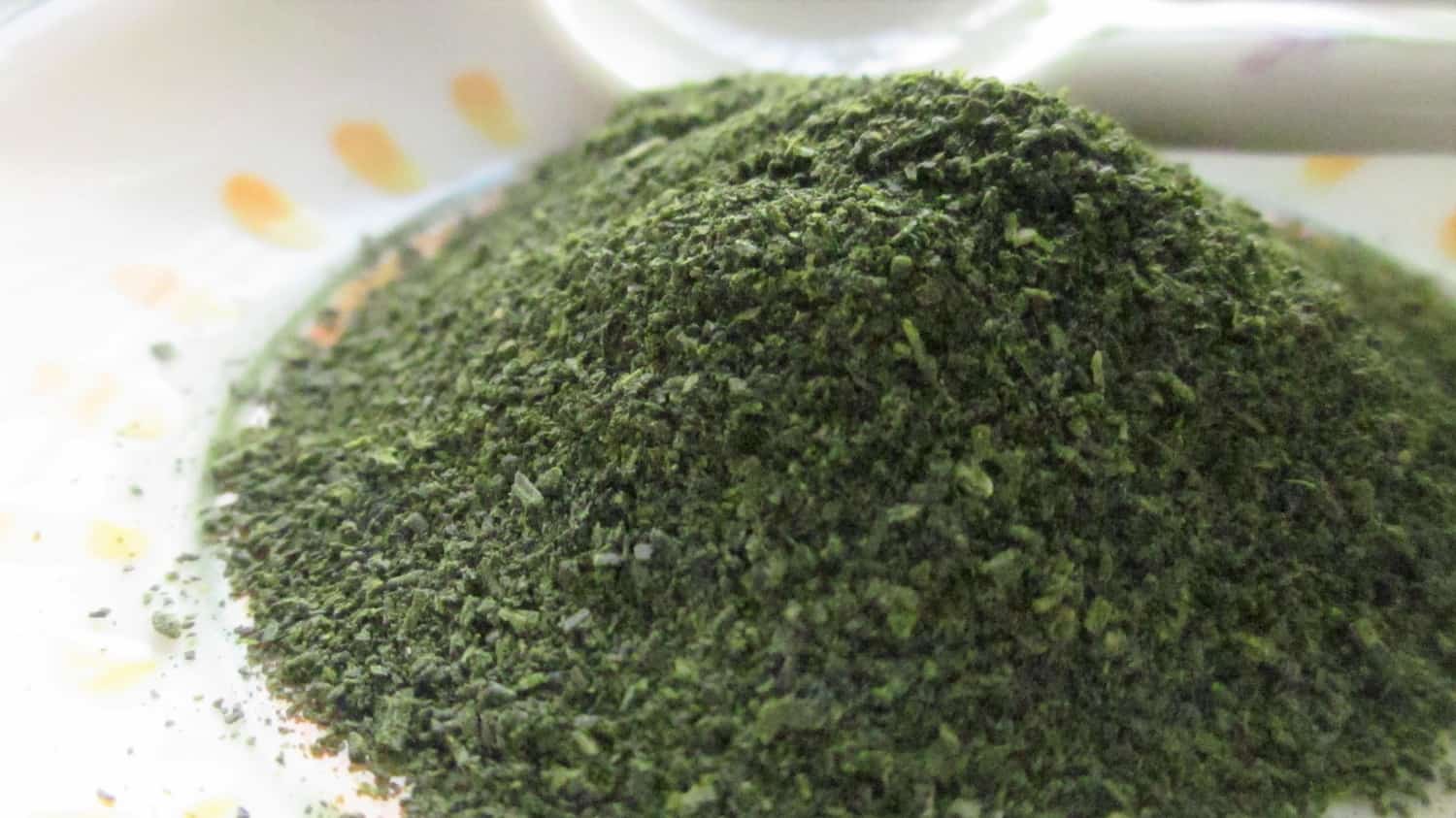 Konacha, fine dark green particles of Japanese green tea, piled on a small white dish