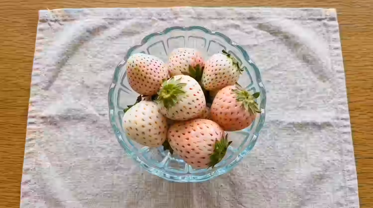 Pearl White strawberries in a scalloped glass bowl on a linen cloth, pale pinkish-white berries with tiny red seeds