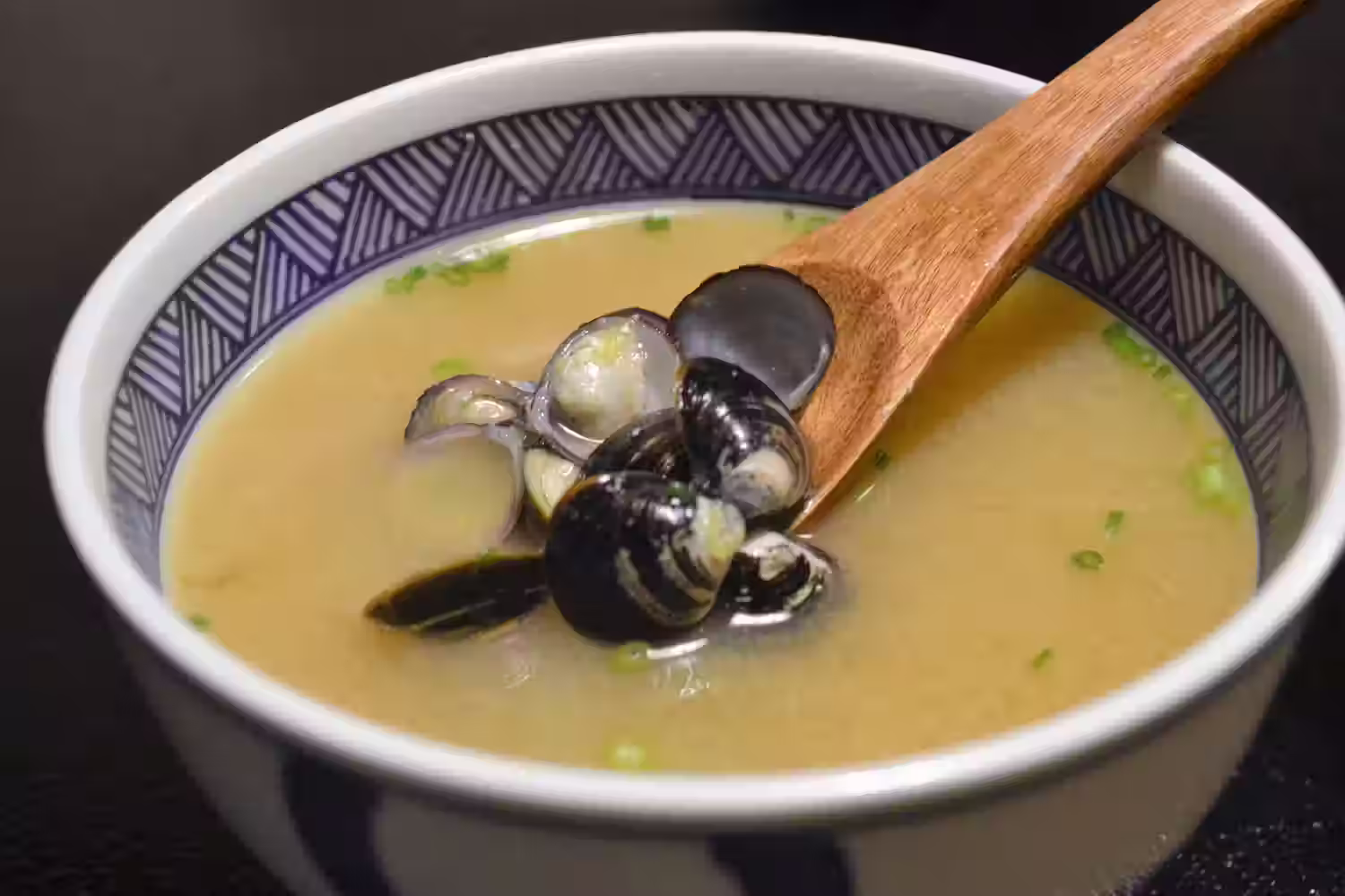 A bowl of Shijimi Jiru miso soup with shijimi clams on a wooden spoon